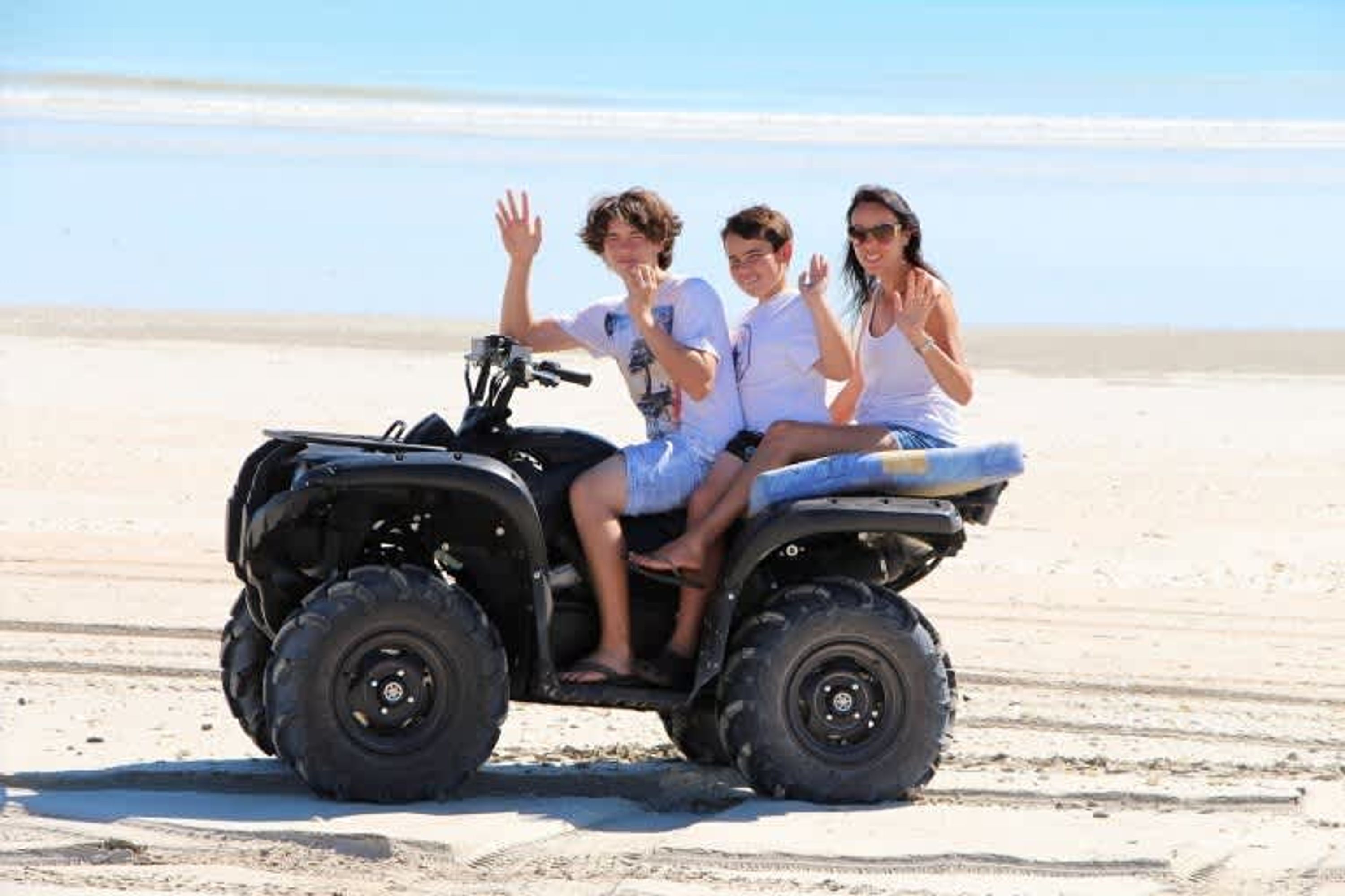 A group of people on an ATV on a sandy beach with a clear sky.