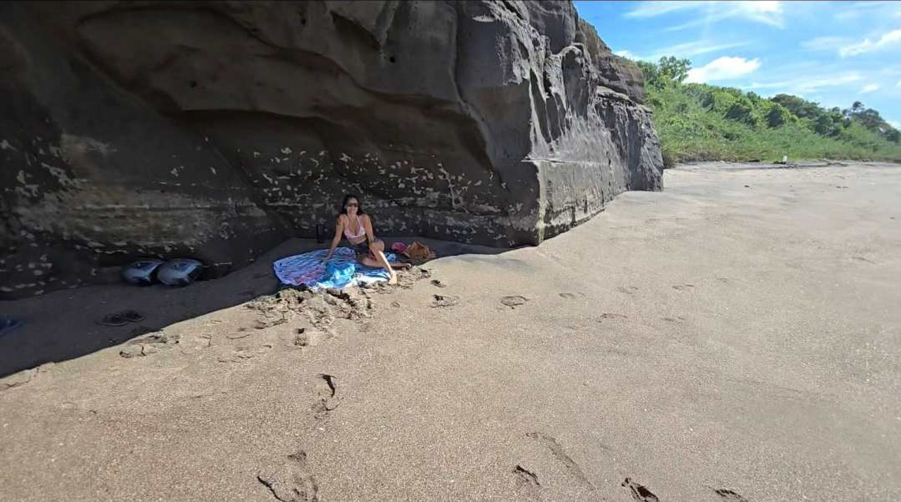 A person sitting on a sandy beach with a large rock formation in the background.