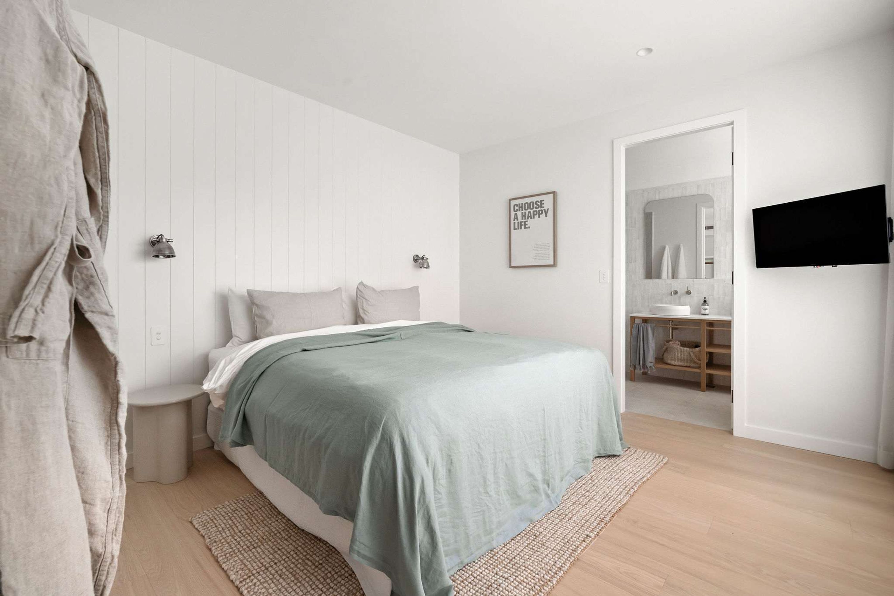 A modern bedroom with a bed, bedside tables, a flat-screen TV, and a framed motivational quote on the wall.