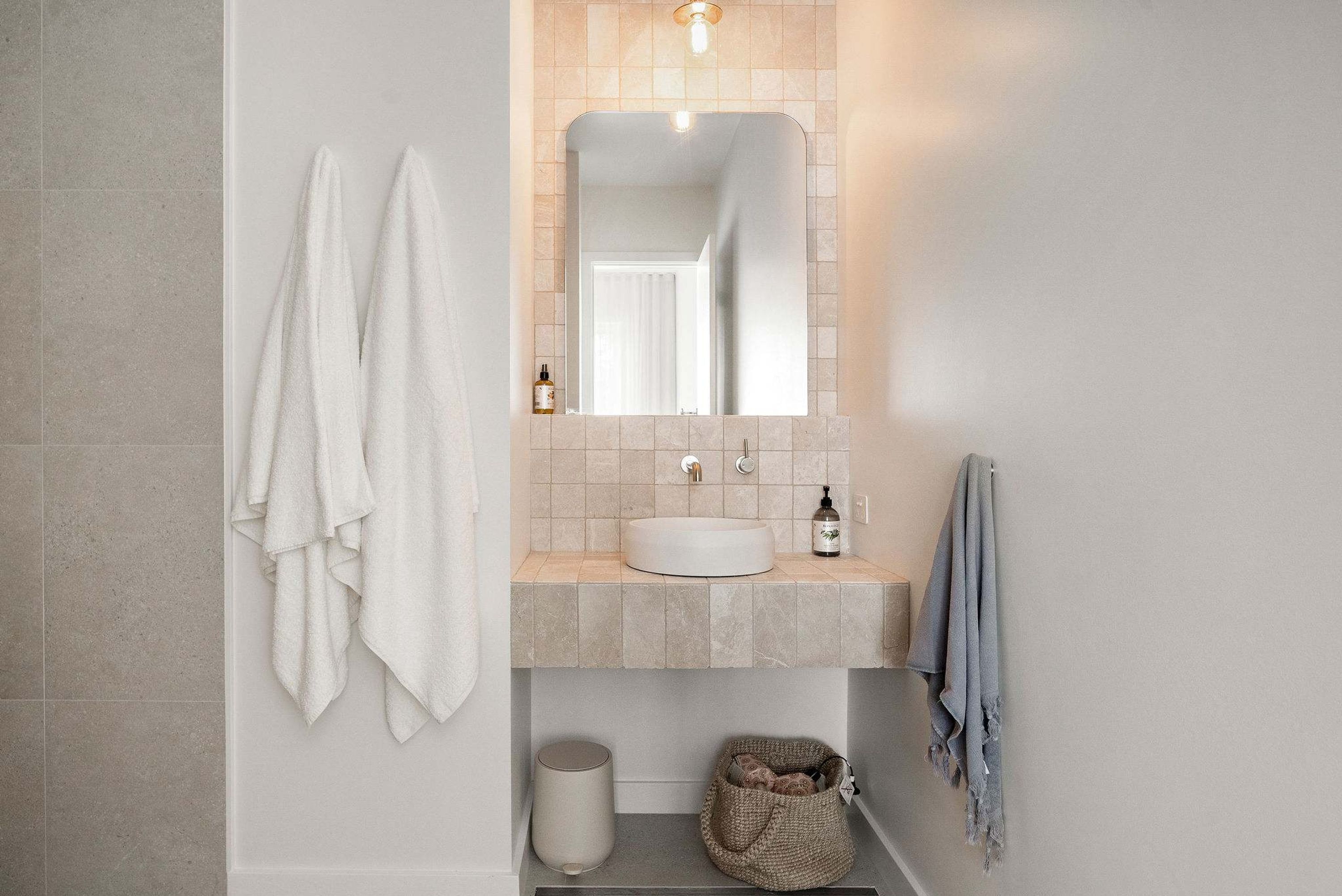 Un baño con un lavabo blanco, un espejo y dos toallas colgadas en la pared.