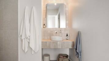 Un baño con un lavabo blanco, un espejo y dos toallas colgadas en la pared.