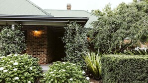 A house with a brick entrance, a well-maintained garden with various plants, and a visible chimney. - Moraea Farm Berry - by Linnaeus Collection (Berry)