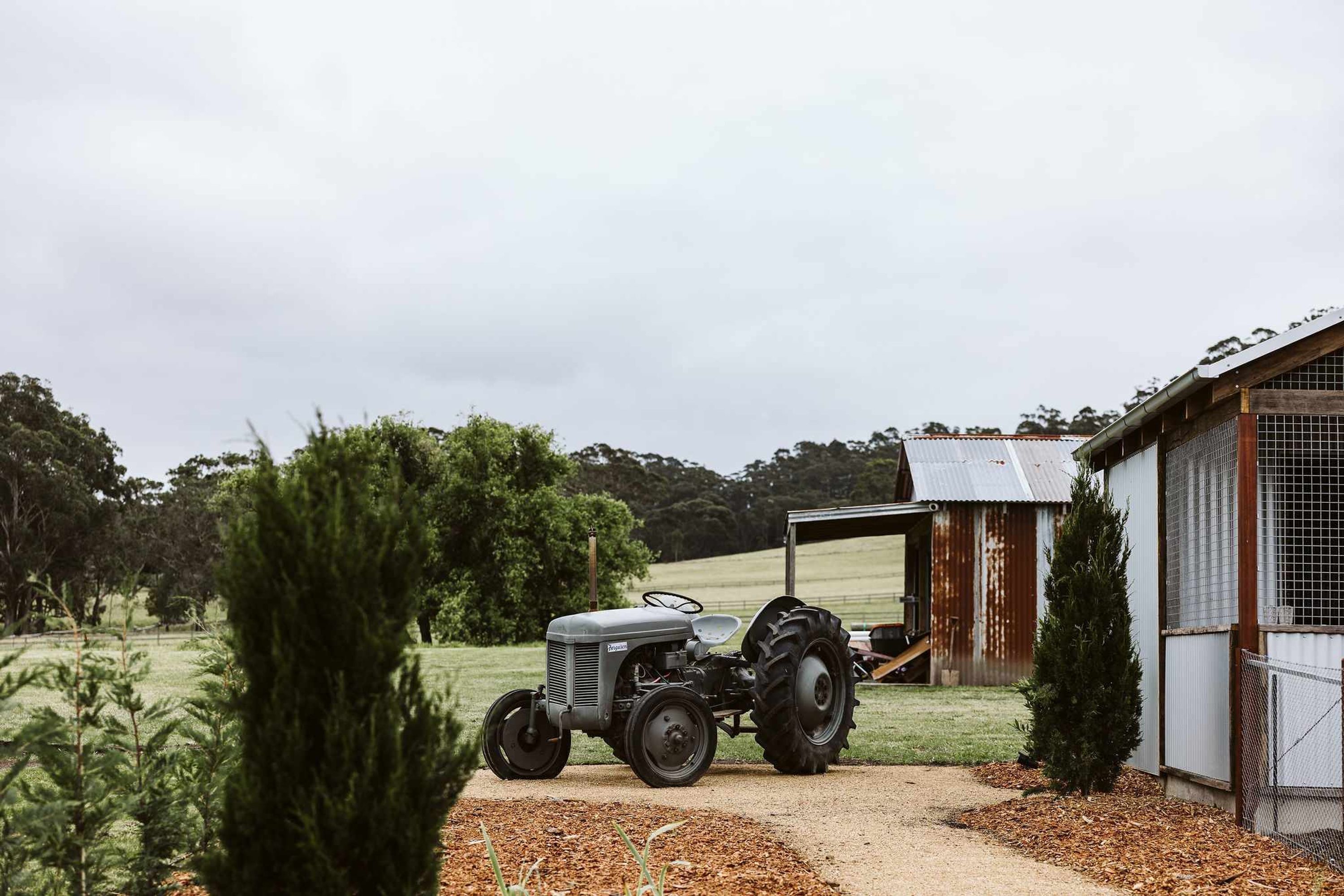 A tractor parked in front of a rustic barn-like structure with a metal roof and wooden walls.