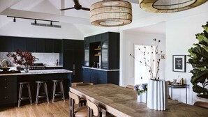 A modern kitchen with dark cabinets, a wooden island with stools, and a large dining table. - Moraea Farm Berry - by Linnaeus Collection (Berry)