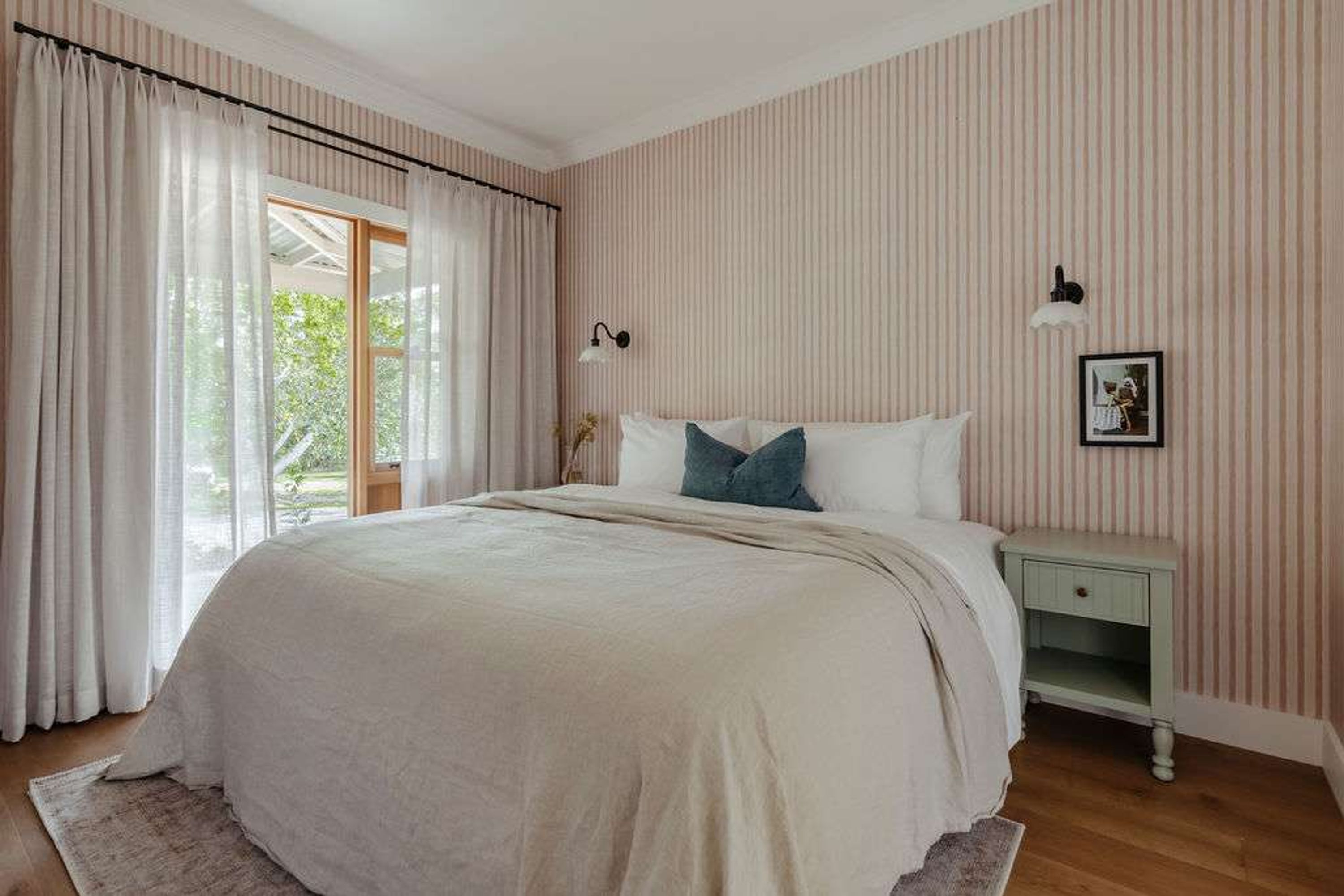 A bedroom with a large bed, a nightstand, a wall-mounted lamp, and a picture on the wall.