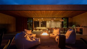 A modern outdoor seating area with a fire feature, wooden deck, and a view into the interior of a contemporary home. - Casa Malbec Valle de Guadalupe (Valle de Guadalupe)