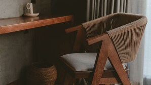 A wooden chair with a cushioned seat and backrest, positioned next to a wooden table and a woven basket. - Casa Malbec Valle de Guadalupe (Valle de Guadalupe)