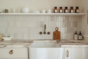 A kitchen with white cabinets, a marble countertop, a sink, and a shelf with jars and bottles. - Moraea Farm Suite in Berry (Berry)