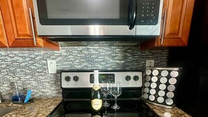 A kitchen with a stainless steel stove, a microwave above it, and a set of silverware and a bottle of champagne on the counter. - Iconic 3BD Home Mins From the Beach Pompano FL (Pompano Beach)
