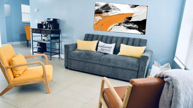 A living room with a grey sofa, yellow armchair, and brown chair. A coffee machine and a small table are in the background. - Iconic 3BD Home Mins From the Beach Pompano FL (Pompano Beach)