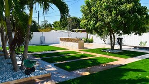 A well-maintained garden with a lawn, a stone planter, and a small wheelbarrow. - Iconic 3BD Home Mins From the Beach Pompano FL (Pompano Beach)
