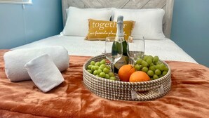 A neatly made bed with a headboard, a bedside table with a bottle and glasses, and a fruit basket on the bed. - Iconic 3BD Home Mins From the Beach Pompano FL (Pompano Beach)