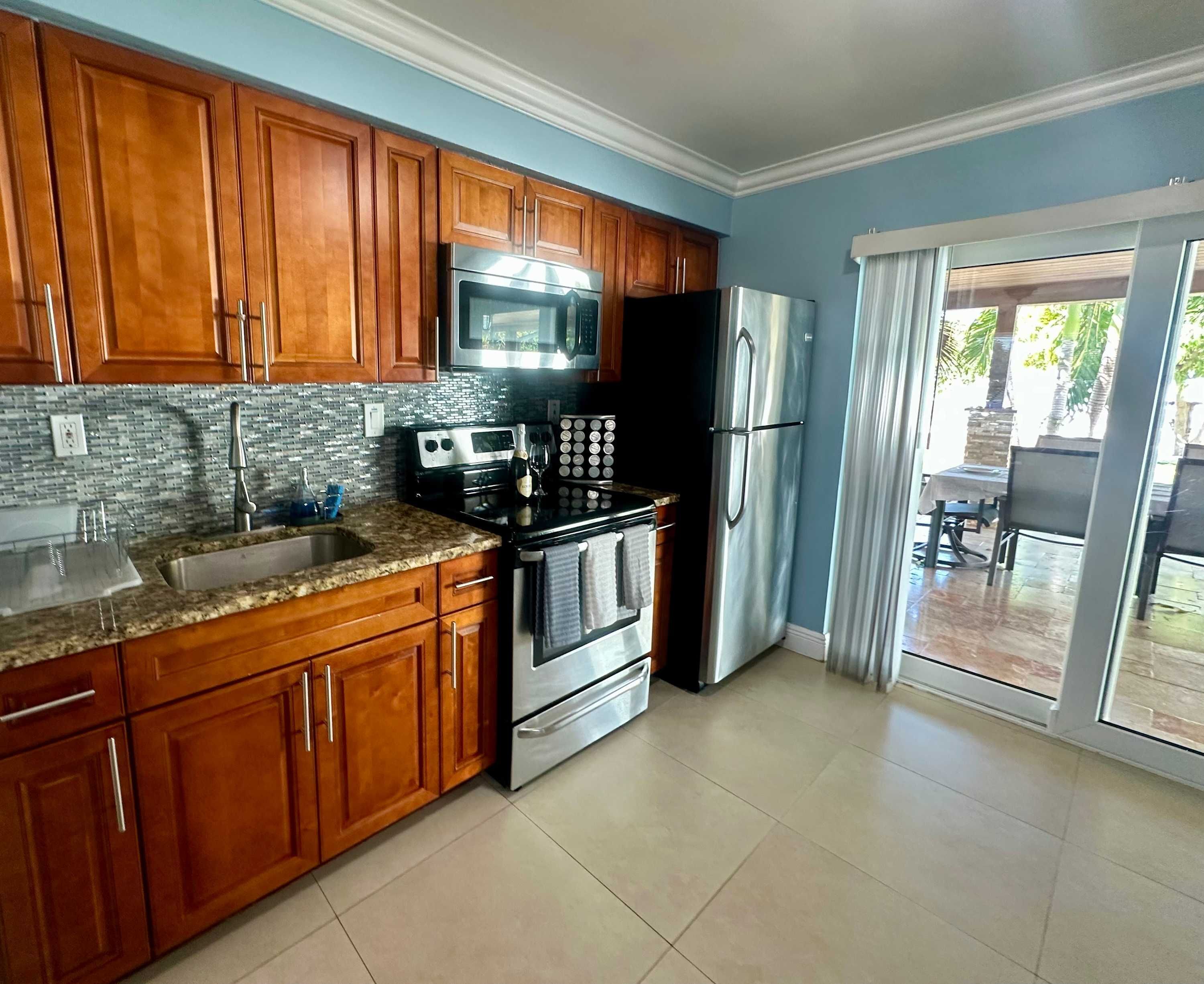 A kitchen with wooden cabinets, stainless steel appliances, a tiled backsplash, and a sliding glass door leading to an outdoor area.