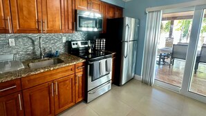 A kitchen with wooden cabinets, stainless steel appliances, a tiled backsplash, and a sliding glass door leading to an outdoor area. - Iconic 3BD Home Mins From the Beach Pompano FL (Pompano Beach)