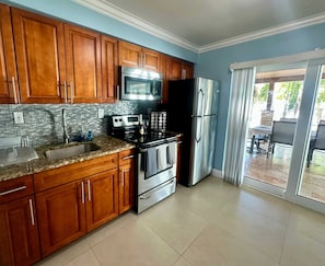 A kitchen with wooden cabinets, stainless steel appliances, a tiled backsplash, and a sliding glass door leading to an outdoor area.