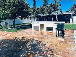 Eine Terrasse im Freien mit Steinboden, Grill und kleinem Poolbereich.