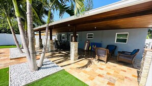 An outdoor patio area with a covered seating area, stone flooring, and palm trees. - Iconic 3BD Home Mins From the Beach Pompano FL (Pompano Beach)