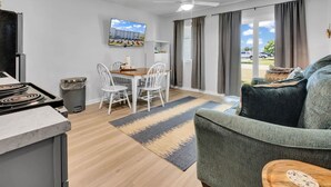 A modern kitchen with a stove, white chairs, a dining table, and a TV on the wall. - Good Vibes - The Affordable Beach Vacay (Gulf Shores)