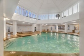 An indoor swimming pool with clear water, surrounded by white walls and large windows. - Good Vibes - The Affordable Beach Vacay (Gulf Shores)