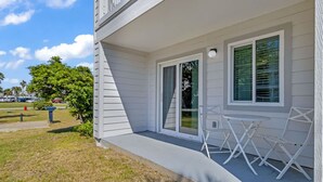 A two-story house with a covered porch, a sliding glass door, and a small outdoor seating area with white chairs. - Good Vibes - The Affordable Beach Vacay (Gulf Shores)