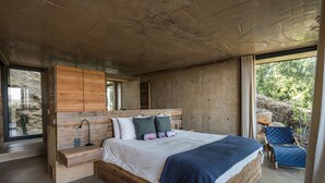 A modern bedroom with a large bed, wooden headboard, and a built-in bench. - Casa UNO - Cuatro Cuatros (Ensenada)