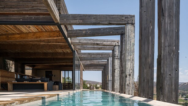 An infinity pool with wooden beams overhead, a seating area with cushions, and a view of the landscape. - Casa UNO - Cuatro Cuatros (Ensenada)