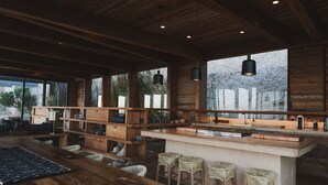 A spacious kitchen with wooden cabinetry, a central island with stools, and large windows offering views of the outdoors. - Casa UNO - Cuatro Cuatros (Ensenada)