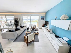 A modern living room with a sofa, armchair, and coffee table, a TV on a white stand, and a balcony with a view. - Modern VIP Villa 100 Privacy Stunning Views (Ermionida)