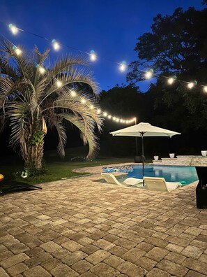 A backyard with a swimming pool, a palm tree, and string lights.