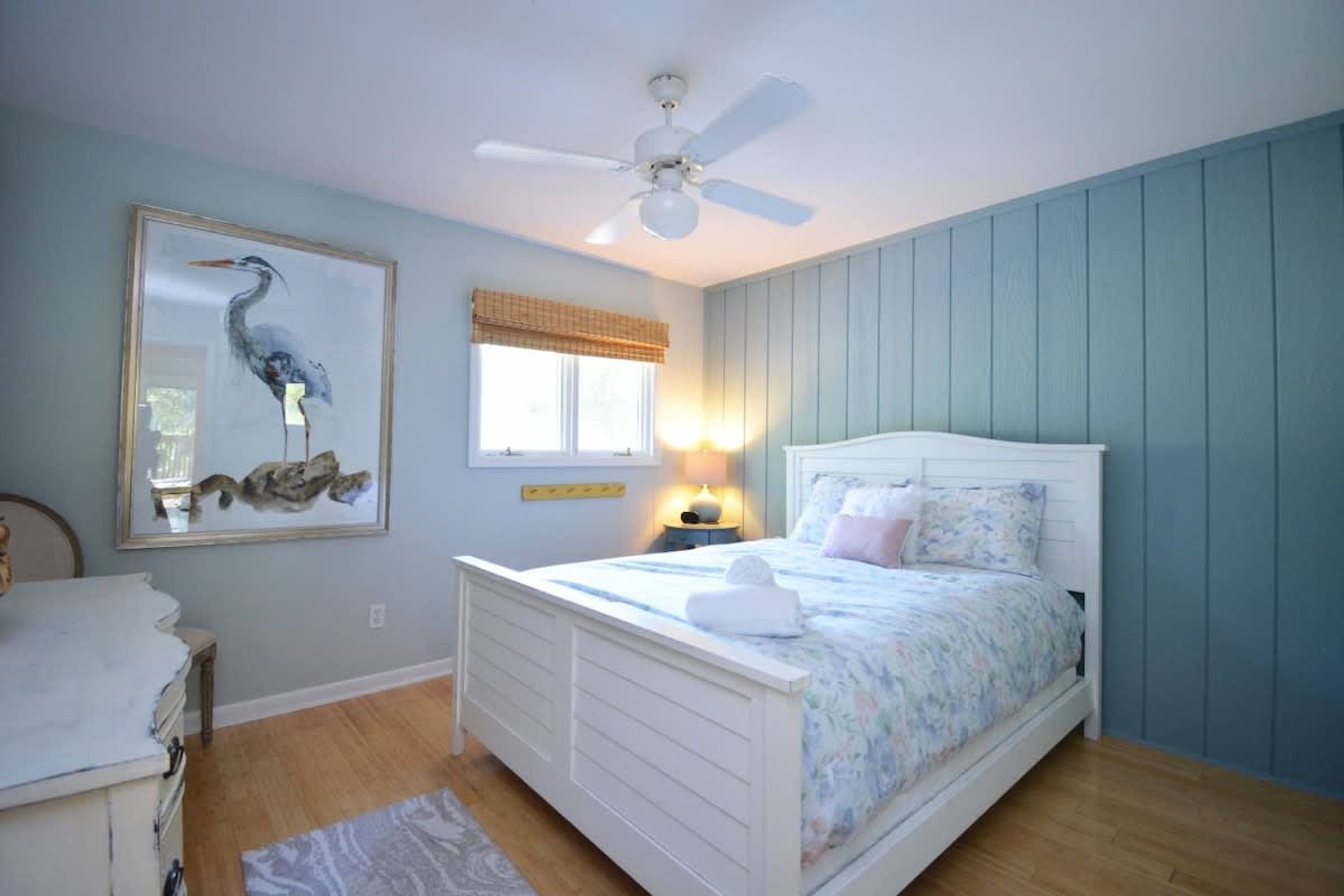 A bedroom with a bed, a ceiling fan, a window with a curtain, and a wall-mounted lamp.