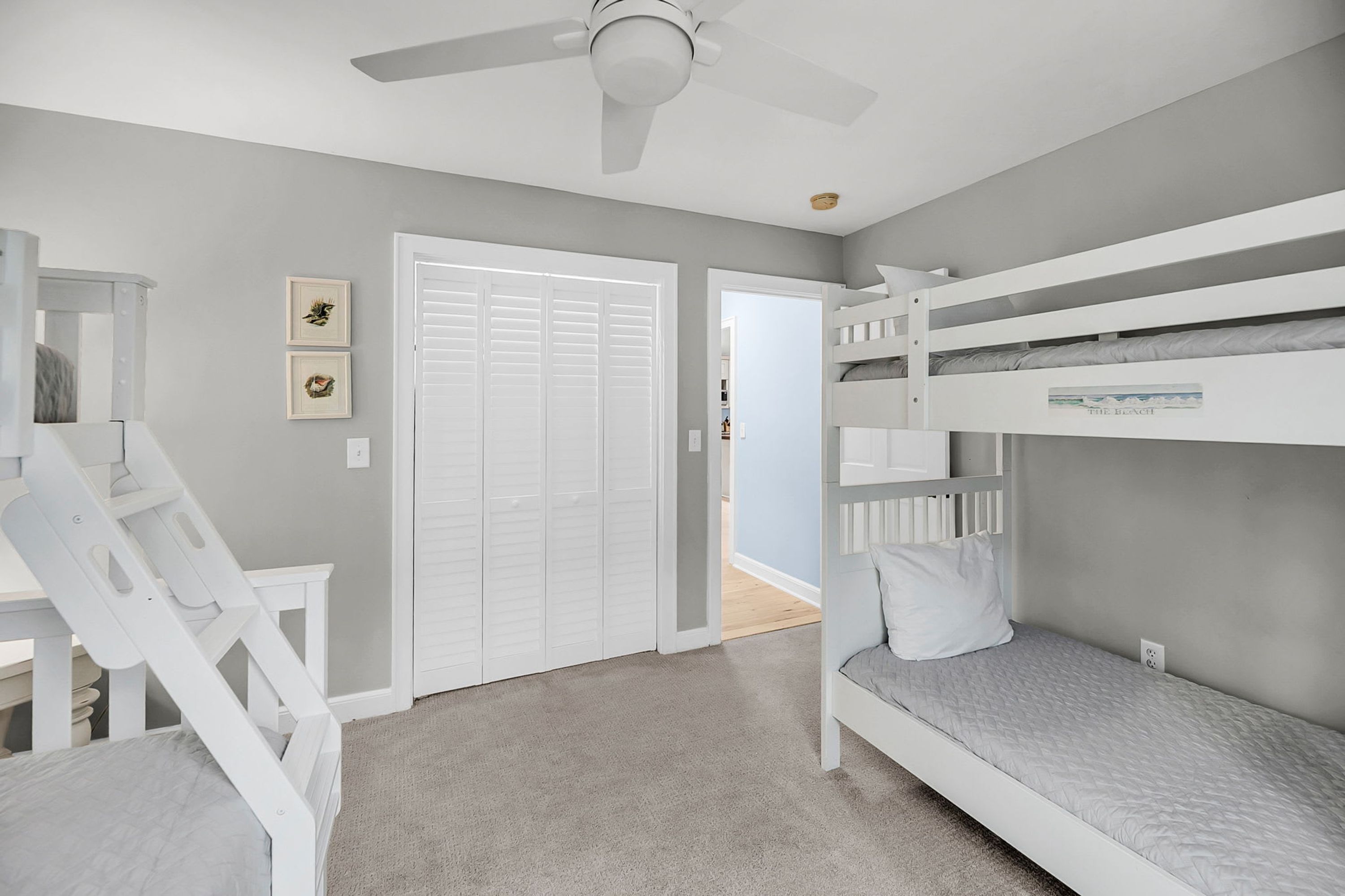 A bedroom with bunk beds, a white chair, a desk, and a ceiling fan.