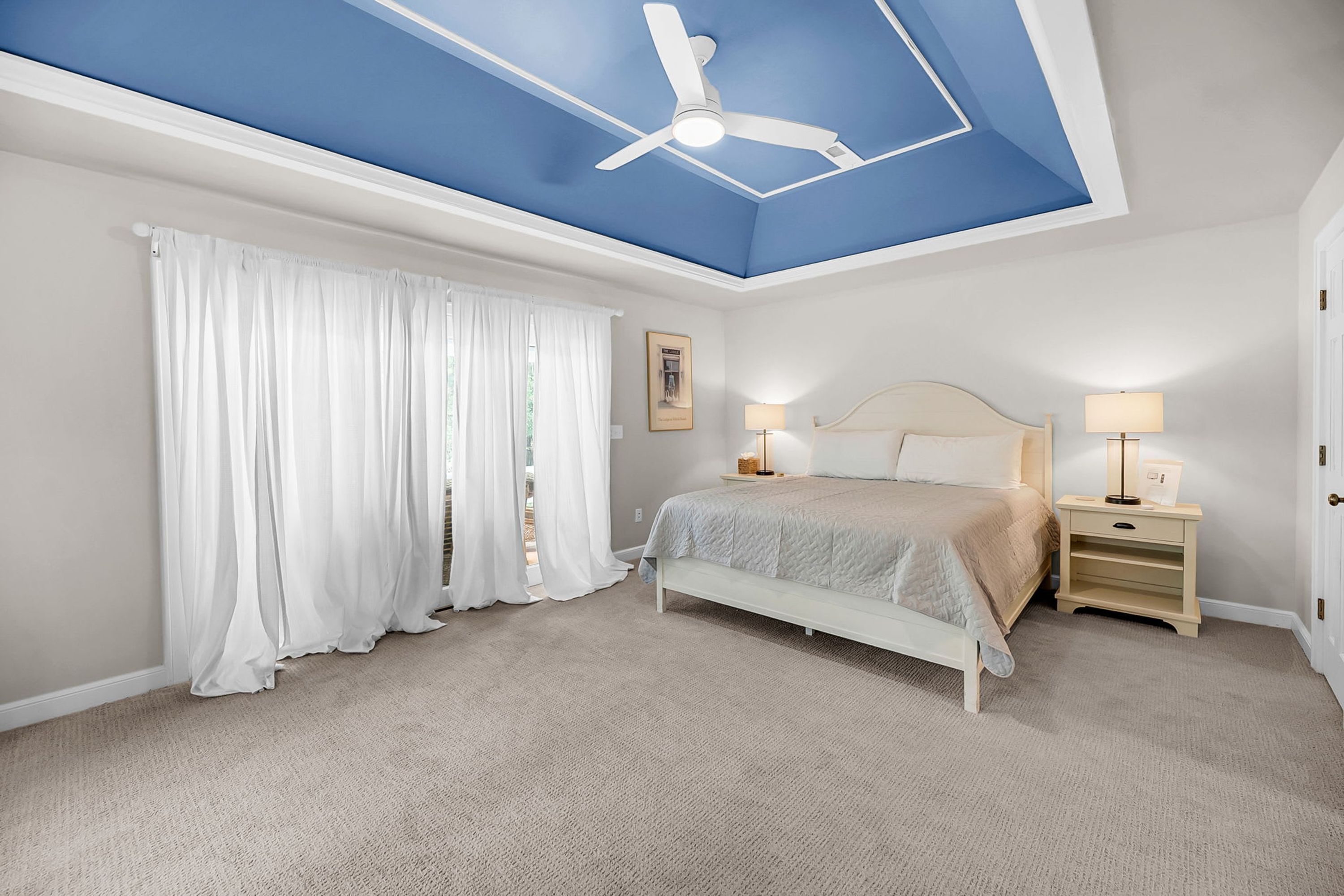 A bedroom with a bed, nightstands, a ceiling fan, and a window with curtains.