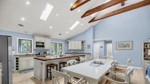 Una cocina amplia con muebles blancos, una isla grande y un comedor con sillas blancas.
