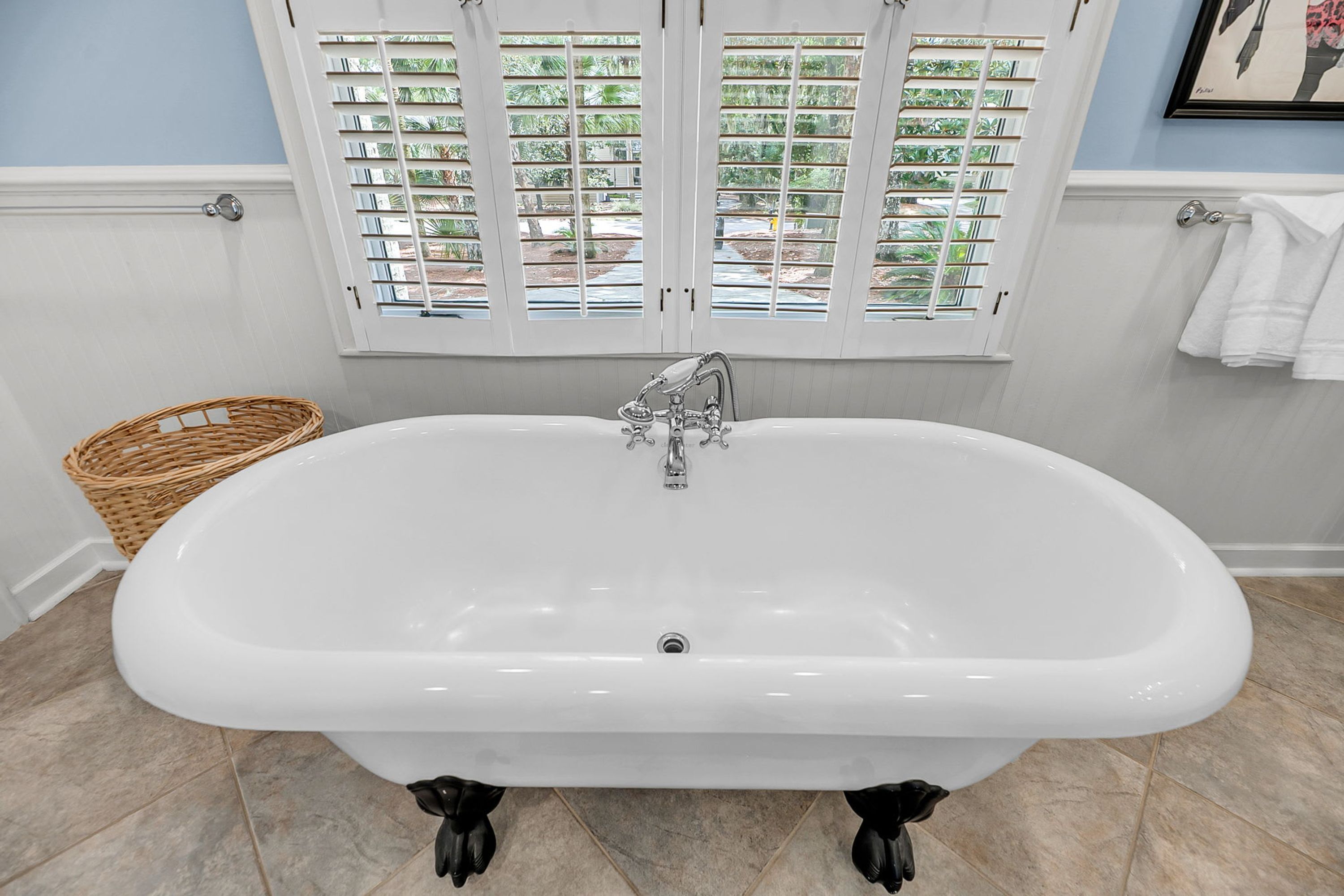 A bathroom with a freestanding bathtub, a wicker basket, and a window with blinds.