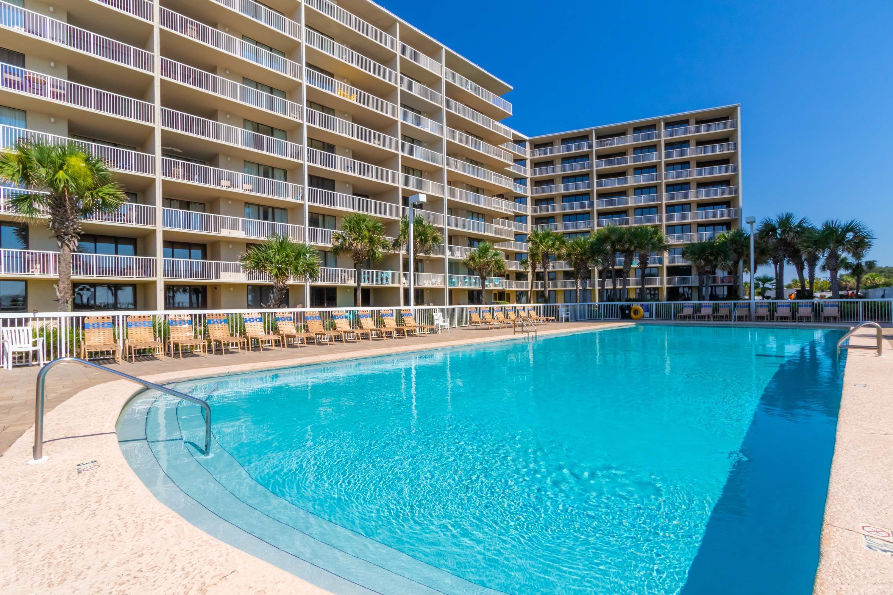 A hotel with a pool, multiple balconies, and palm trees.