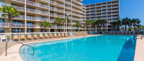 A hotel with a pool, multiple balconies, and palm trees.