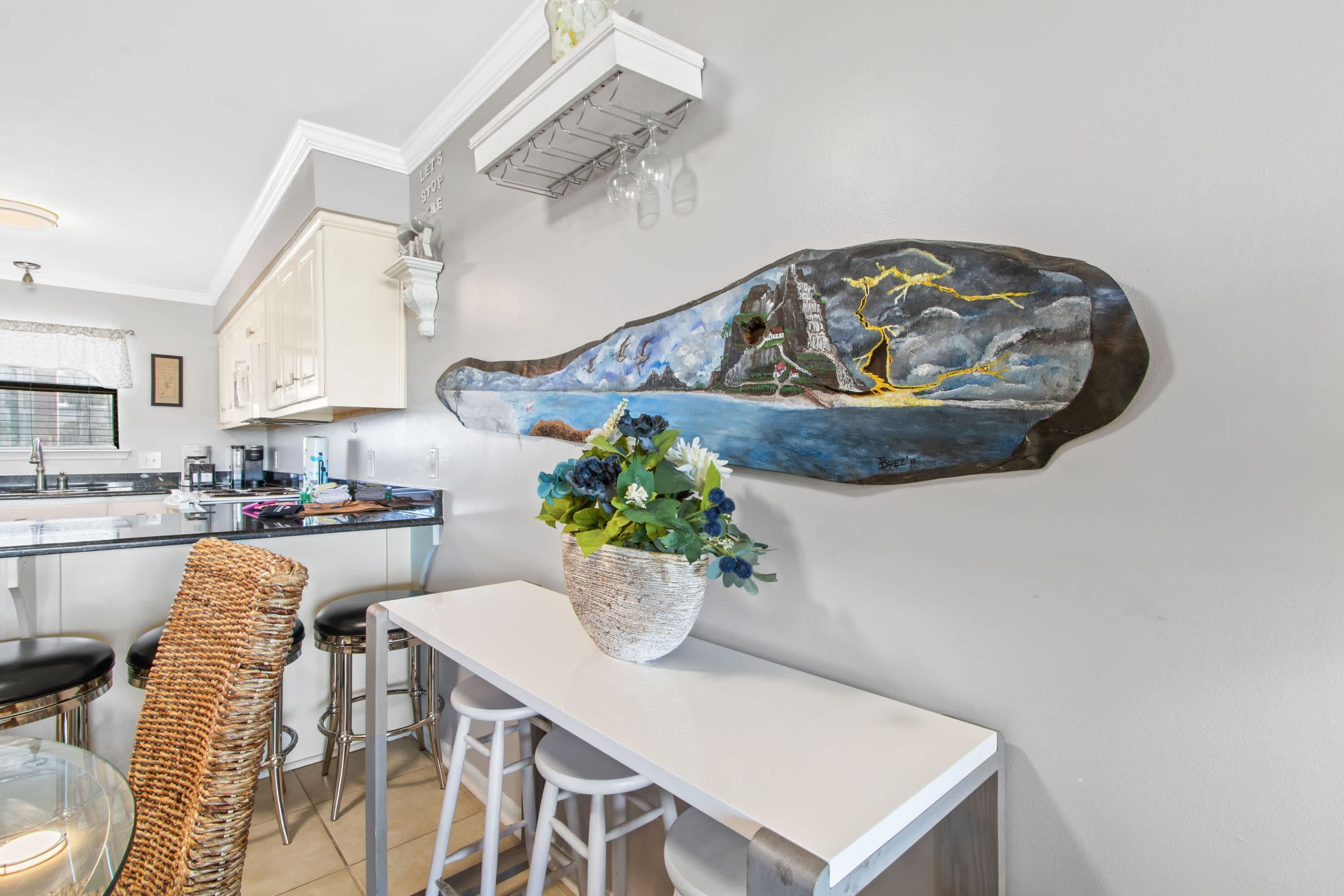 A modern kitchen with white cabinets, a large island, and a painting of a landscape on the wall.