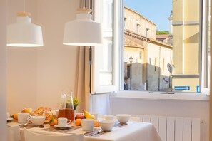 A breakfast table with croissants, fruits, and coffee cups by a window with a view of buildings. - Colosseum Holidays - San Giovanni in Laterano (Rome)