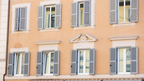 Fachada de edificio con varias ventanas, contraventanas y un frontón decorativo.