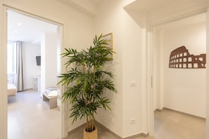 Um corredor com uma planta de bambu em vaso, um quadro na parede e um recorte de um edifício na parede adjacente.