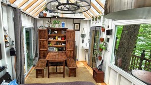 Une cuisine compacte avec une table et des bancs en bois, une bibliothèque intégrée et une grande fenêtre donnant sur un espace verdoyant.
