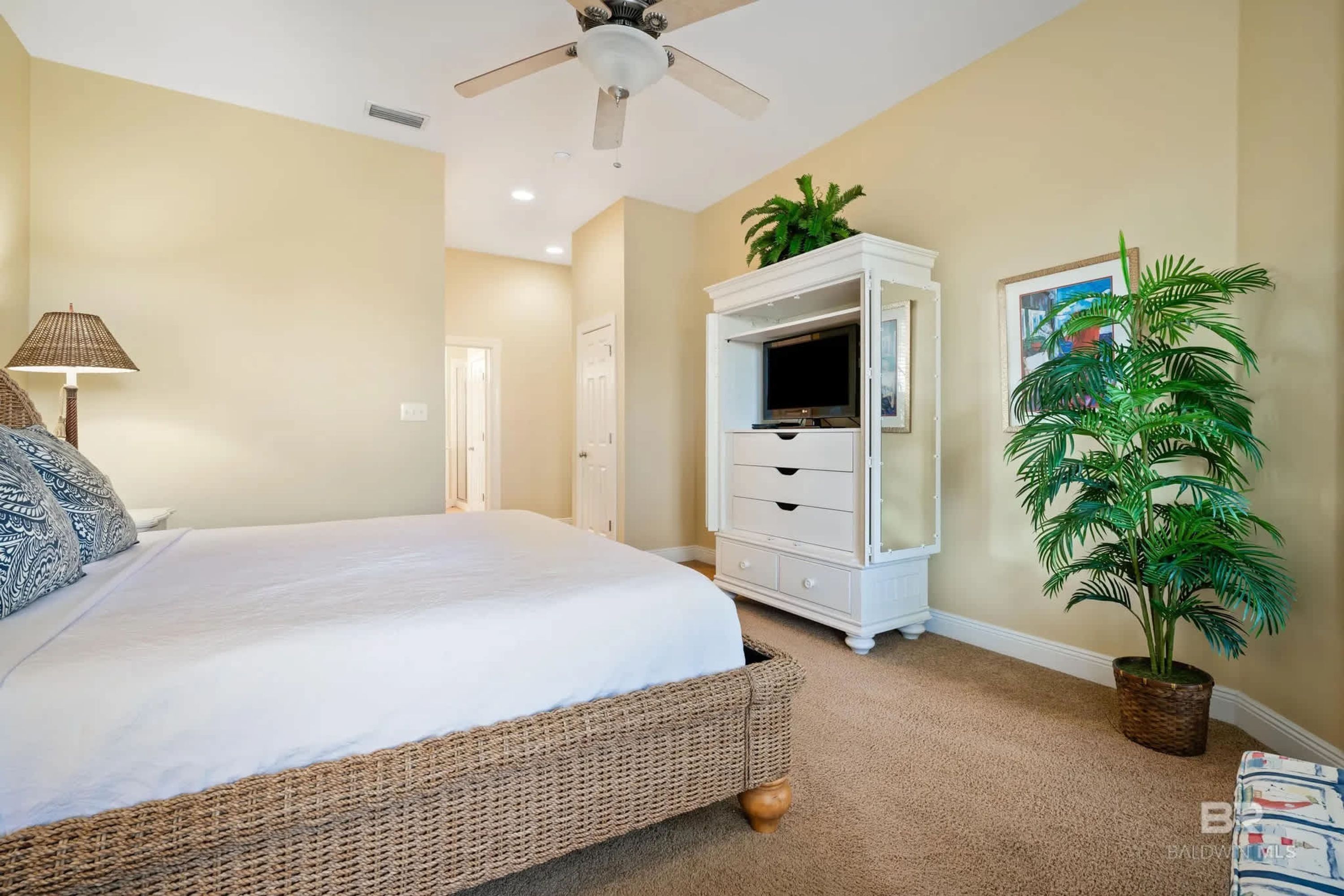 A bedroom with a bed, a ceiling fan, a TV cabinet, and a potted plant.