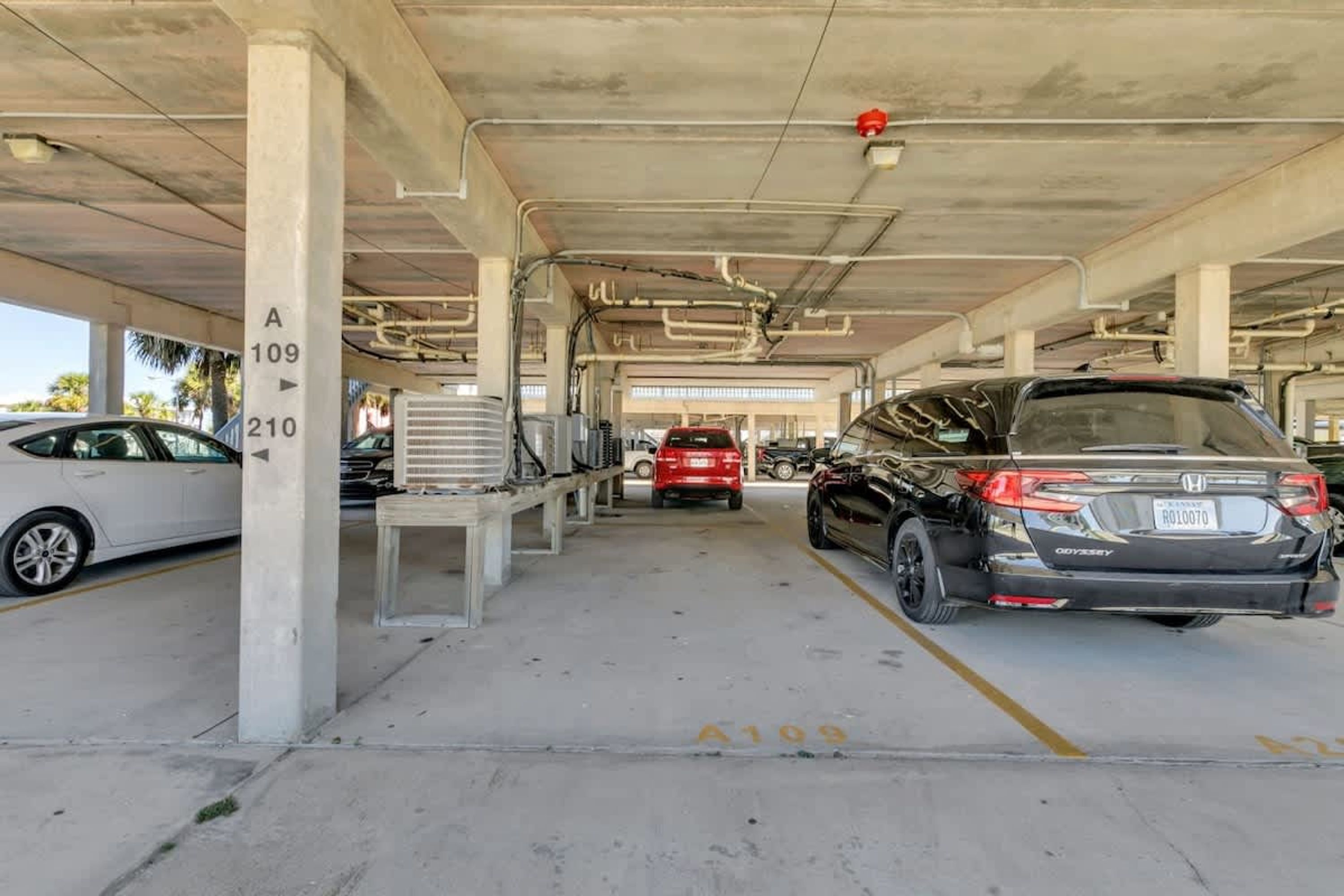 A parking garage with concrete pillars, marked parking spaces, and a red car in the distance.
