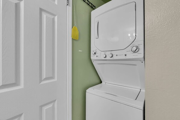 Una lavadora blanca en una habitación con una puerta blanca y paredes verdes.