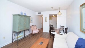 Un salon comprenant un canapé, une table basse en bois, une table à manger avec des chaises, un meuble et un fauteuil à motifs.
