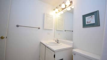 A bathroom with a white sink, a mirror with lights, a towel rack, and a framed picture on the wall.