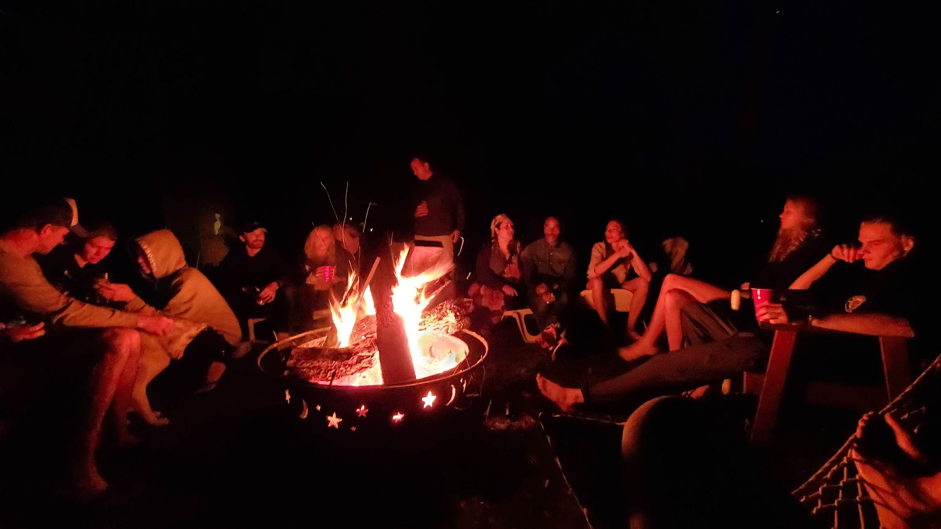 Un groupe de personnes s’est rassemblé autour d’un feu de camp au coucher du soleil.