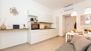 A modern kitchen with white cabinetry, an oven, and a dining area with a table and chairs. - Colosseum Holidays - Marco Aurelio (Rome)