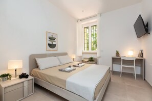 Une chambre à coucher moderne, équipée d’un lit, de tables de chevet, d’un bureau et d’un téléviseur fixé au mur.