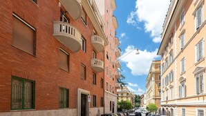 A narrow urban street with multi-story buildings, balconies, and a clear sky. - Colosseum Holidays - Marco Aurelio (Rome)